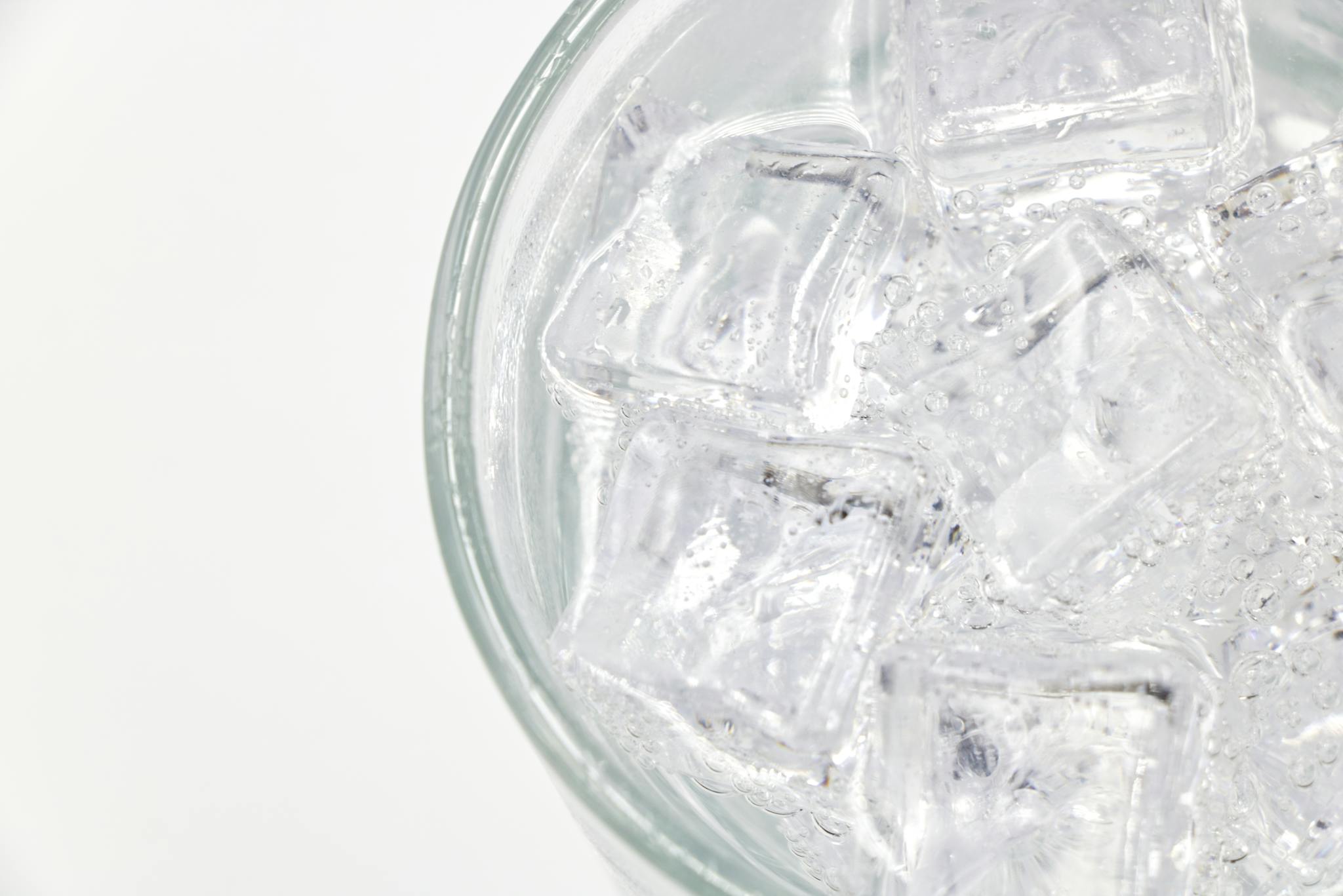 Close-up of a glass filled with sparkling water and ice cubes on a white background.