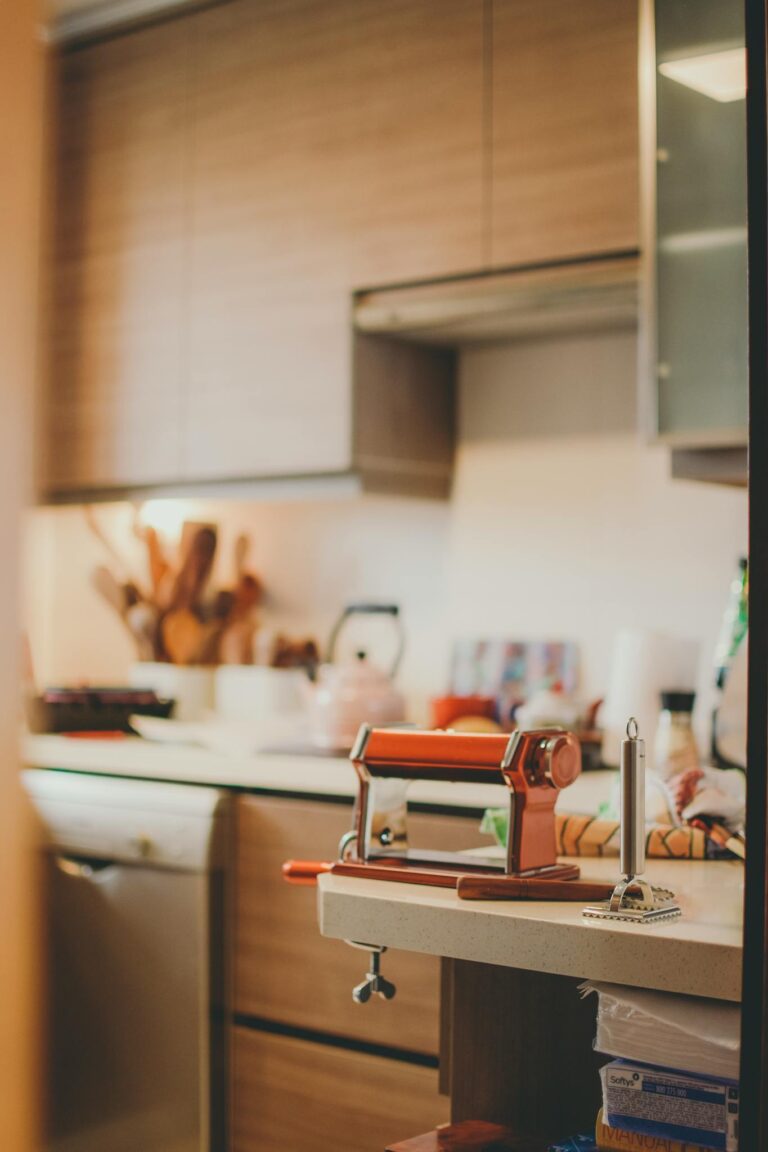 Warm kitchen featuring a pasta maker on a countertop, surrounded by wooden utensils and soft natural light.